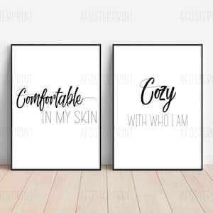 May include: Two black framed prints with white backgrounds. The print on the left says "Comfortable in my skin". The print on the right says "Cozy with who I am".