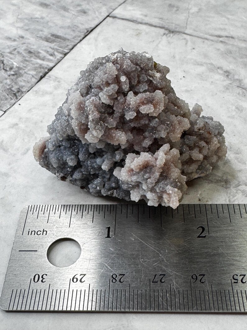 May include: A cluster of purple and gray amethyst crystals, measuring approximately 1 inch in diameter, on a ruler for scale.