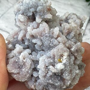 May include: A cluster of small, white and purple crystals with a rough, textured surface. The crystals are clustered together in a dense, irregular shape.
