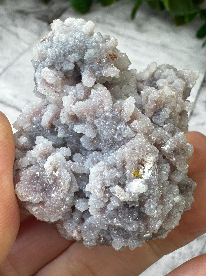 May include: A cluster of small, white and purple crystals with a rough, textured surface. The crystals are clustered together in a dense, irregular shape.