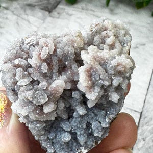 May include: A cluster of gray and purple amethyst crystals with a rough, textured surface. The crystals are clustered together in a heart shape.