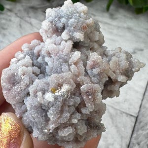 May include: A cluster of small, white and gray crystals with a rough, textured surface. The crystals are clustered together in a random, organic shape.