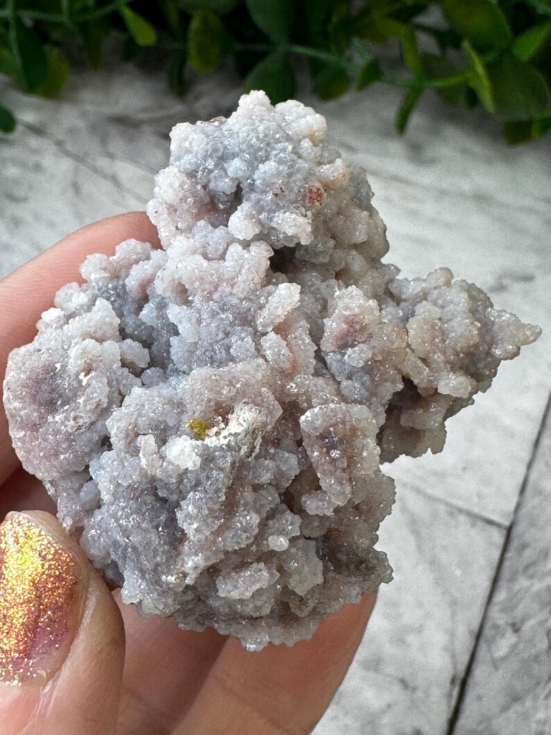 May include: A cluster of small, white and gray crystals with a rough, textured surface. The crystals are clustered together in a random, organic shape.