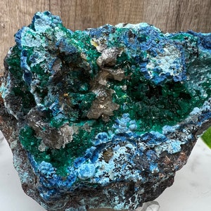 May include: A close-up of a natural mineral specimen. The rock features a mix of deep blues, vibrant greens, and hints of brown. The surface has a textured, crystalline appearance, with areas of sparkling crystal formations.