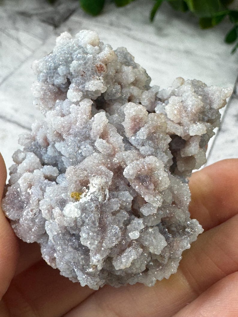 May include: A cluster of small, white, and gray crystals with a slightly pink hue. The crystals are clustered together in a rough, organic shape.