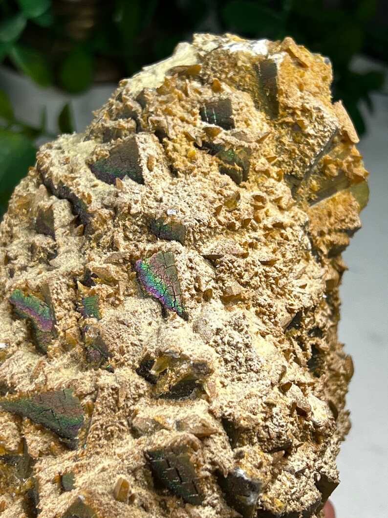 May include: A close-up of a brown and gold iridescent mineral specimen with a rough, textured surface. The mineral has a crystalline structure with many small, sharp points.