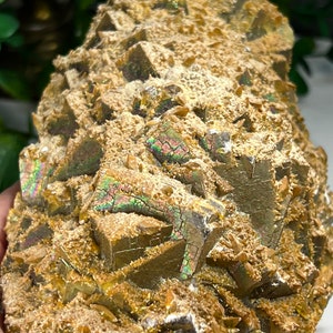 May include: A cluster of iridescent, golden-brown crystals with a rough, textured surface. The crystals are arranged in a pyramid shape, with some of the crystals showing a rainbow sheen.
