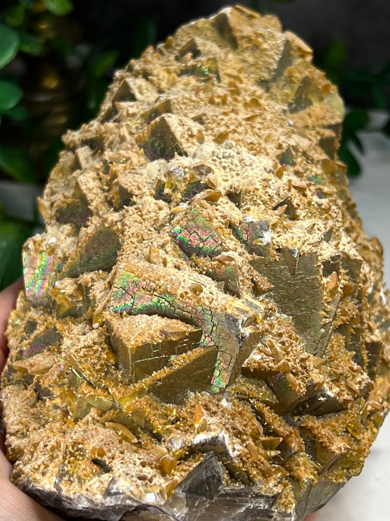 May include: A cluster of iridescent, golden-brown crystals with a rough, textured surface. The crystals are arranged in a pyramid shape, with some of the crystals showing a rainbow sheen.