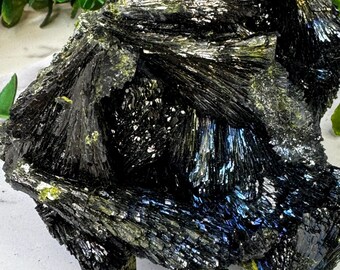 May include: A cluster of black, iridescent, and green crystals with a rough, natural texture. The crystals are arranged in a jagged, organic shape.