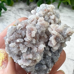 May include: A cluster of gray and white chalcedony with a rough, textured surface. The chalcedony has a crystalline structure and is a natural gemstone.