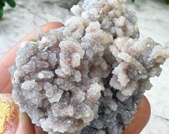 Op de afbeelding: Een cluster van grijze en witte chalcedoon met een ruw, getextureerd oppervlak. De chalcedoon heeft een kristallijne structuur en is een natuurlijke edelsteen.