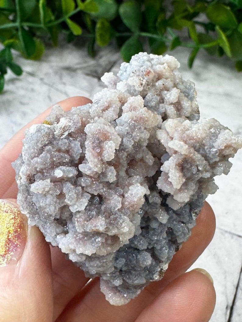 May include: A cluster of gray and white chalcedony with a rough, textured surface. The chalcedony has a crystalline structure and is a natural gemstone.