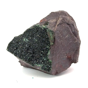 May include: A rough, reddish-brown rock formation with a dark, sparkling, black mineral deposit. The mineral deposit has small, green accents. The rock is set against a white background.