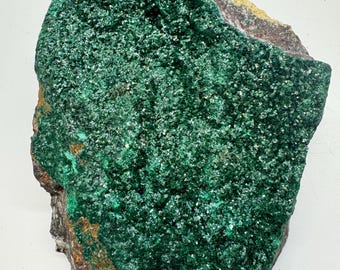 May include: A rough-hewn, natural malachite specimen. The surface is covered in a vibrant, textured, deep green crystalline formation. The edges reveal a mix of brown, gray, and yellow hues, creating a striking contrast. This mineral sample is ideal for collectors.