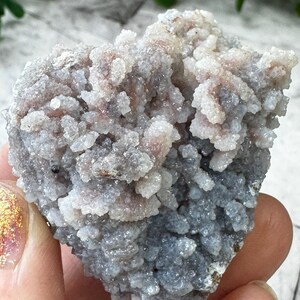 May include: A cluster of gray and pink chalcedony crystals with a rough, textured surface. The crystals are clustered together in a dense, irregular shape.