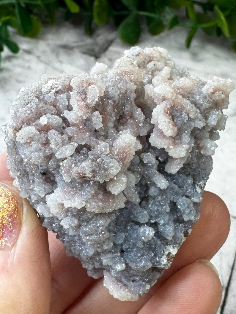 May include: A cluster of gray and pink chalcedony crystals with a rough, textured surface. The crystals are clustered together in a dense, irregular shape.