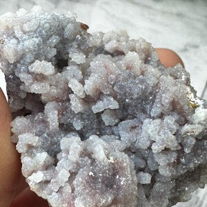 May include: A cluster of small, white and purple crystals with a rough, natural texture. The crystals are densely packed together, creating a unique and interesting pattern.
