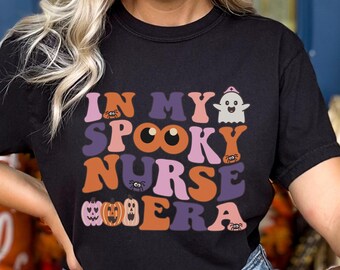 Może przedstawiać: Czarny T-shirt z nadrukiem graficznym, który mówi "In My Spooky Nurse Era" z ilustracjami ducha, pająka i dyni.