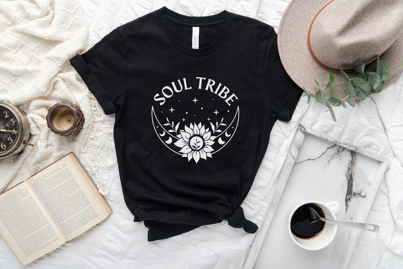 May include: Black t-shirt with a white graphic design of a crescent moon with a sunflower inside and the text "SOUL TRIBE" above it.