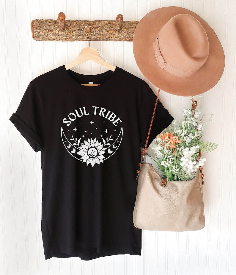 May include: Black t-shirt with a white graphic design of a sunflower inside a crescent moon with stars. The text "SOUL TRIBE" is above the design.