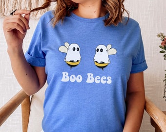 May include: A light blue t-shirt featuring a graphic of two cartoon bees dressed as ghosts. The bees have white ghost costumes, yellow and black stripes, and small wings. The text "Boo Bees" is printed below the bees in white.