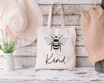 May include: A white tote bag with black handles and a black and white bee illustration. The bag has the word "Kind" printed on it.