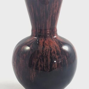 May include: A small, glossy vase with a rounded base and a flared top. The vase has a dark brown and black color scheme with a unique, streaked pattern. The vase is approximately 6 inches tall.