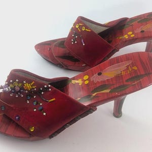 Könnte beinhalten: Ein Paar rote Mules mit Absätzen und Blumendesign auf den Sohlen. Die Oberteile sind dunkelrot mit Perlenverzierungen. Die Absätze sind etwa 7,6 cm hoch.