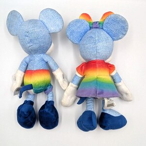 May include: Two plush toys of a mouse character, one with a rainbow-colored tail and the other with a rainbow dress and bow. Both toys have blue denim-like fabric for their bodies, large ears, and white gloves.