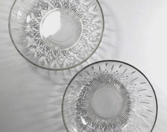 May include: Two clear glass bowls featuring a radial pattern of etched lines and diamond-shaped facets radiating from a smooth circular center. The bowls have a transparent finish and a circular rim, showcasing a detailed pressed glass design.