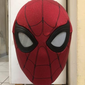May include: A red Spider-Man mask with black accents around the eyes. The mask has a textured surface and a web pattern design. The eye openings are white with a mesh material.