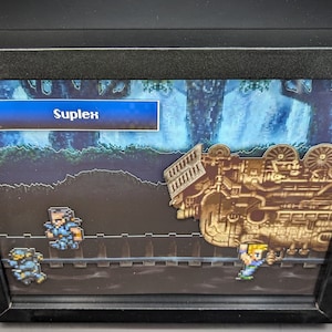 May include: A framed 3D pixel art scene from a video game. The scene depicts a train car, a character in blue armor, and a character in green armor. The text "Suplex" is displayed in a blue box at the top of the image.