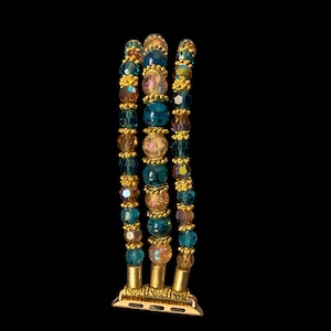 May include: An Apple Watch band featuring three strands of colorful beads. The beads are a mix of teal, gold, and pink, with gold accents. The band has a gold-colored metal connector.