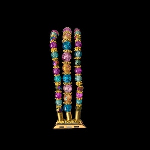 May include: A multi-strand Apple Watch band with colorful beads. The band features strands of purple, teal, pink, and gold beads. The band has gold-colored connectors and is set against a black background.