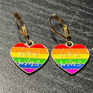 May include: A pair of gold heart-shaped earrings with a rainbow enamel design and the words "love wins" written in white.