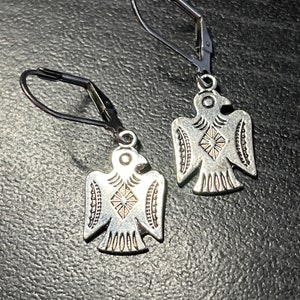 May include: A pair of silver eagle earrings with a geometric design. The earrings have a leverback closure.