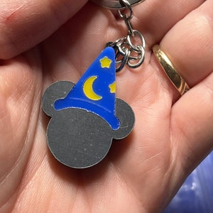 May include: A silver key chain with a blue and yellow Mickey Mouse head charm. The charm features Mickey Mouse wearing a blue wizard hat with yellow stars and a crescent moon.