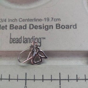 May include: A silver angel wing earring with a clear crystal in the center. The earring is on a white bead design board with the text "3/4 Inch Centerline-19.7cm Jet Bead Design Board bead landing&trade;".