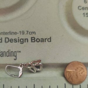 May include: Silver angel wing earring with a hook closure. The earring is about 1 inch long and is shown next to a US penny for size comparison.
