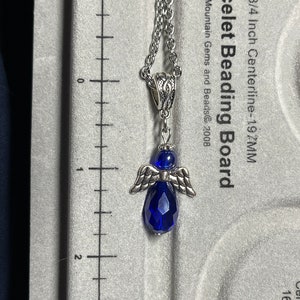 Pu&ograve; includere: Una collana con catena d'argento con un ciondolo a forma di angelo in cristallo blu. Il ciondolo ha un diametro di 5 cm. La catena &egrave; lunga 19,7 cm.
