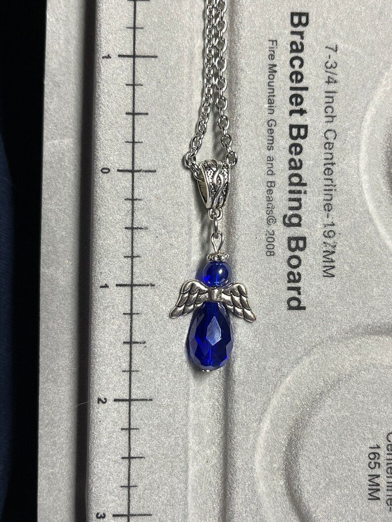 Pu&ograve; includere: Una collana con catena d'argento con un ciondolo a forma di angelo in cristallo blu. Il ciondolo ha un diametro di 5 cm. La catena &egrave; lunga 19,7 cm.