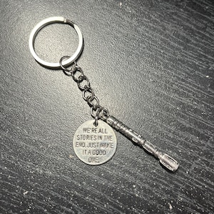 May include: Silver keychain with a round charm that says "We're all stories in the end. Just make it a good one." and a small silver replica of a sonic screwdriver.