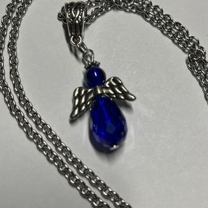 Pu&ograve; includere: Una collana a catena d'argento con un ciondolo a forma di angelo in cristallo blu. L'angelo ha ali d'argento e un corpo a forma di lacrima.