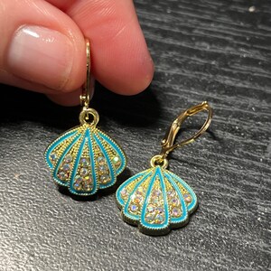 May include: A pair of gold tone earrings with a blue and gold seashell design. The seashells are accented with clear rhinestones.