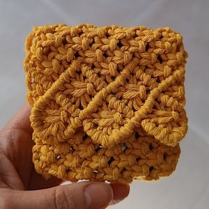 Op de afbeelding: Een klein, geel gehaakt tasje met een geometrisch patroon. Het tasje is gemaakt van dik garen en heeft een licht getextureerd oppervlak.