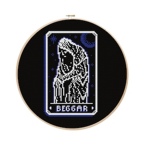 May include: A black and white cross-stitch embroidery hoop with a design of a person in a hooded robe with the word "BEGGAR" at the bottom.