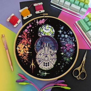 May include: A black and white cross-stitch pattern of a spaceship in space with a colourful nebula background. The spaceship is surrounded by stars and planets. The pattern is framed in a wooden hoop.