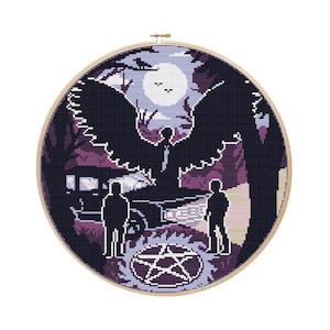 May include: A cross-stitch embroidery hoop featuring a scene with two figures, a car, and a large winged figure. The design uses shades of purple, black, and white, with a full moon in the background. A pentagram is at the bottom.