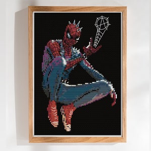 Puede incluir: Un diseño de punto de cruz de pixel art de un personaje Spider-Man rojo y azul con un lanzador de telarañas en un marco negro.