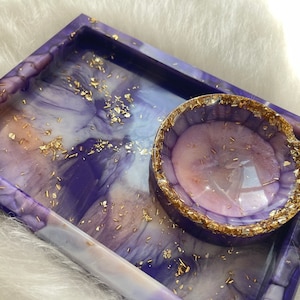 May include: A purple and white resin tray with gold flecks and a matching smaller dish. The tray has a marbled effect and the dish has a smooth surface.